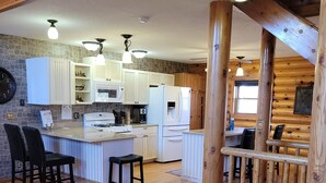 A spacious kitchen with white cabinets, a central island, and a wooden staircase. - Log Cabin located minutes from Missouri River, airport, I-90 and downtown. (Chamberlain)