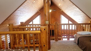 A loft bedroom with a sloped ceiling, wooden beams, a bunk bed, and a window providing natural light. - Log Cabin located minutes from Missouri River, airport, I-90 and downtown. (Chamberlain)