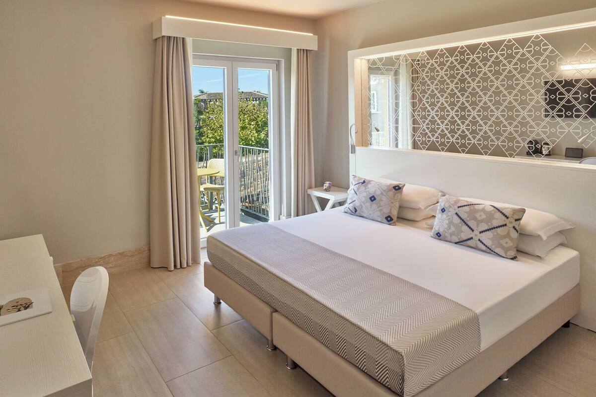 Een hotelkamer met een bed, een bureau, een stoel, een koffiezetapparaat en uitzicht op het landschap door een schuifdeur.