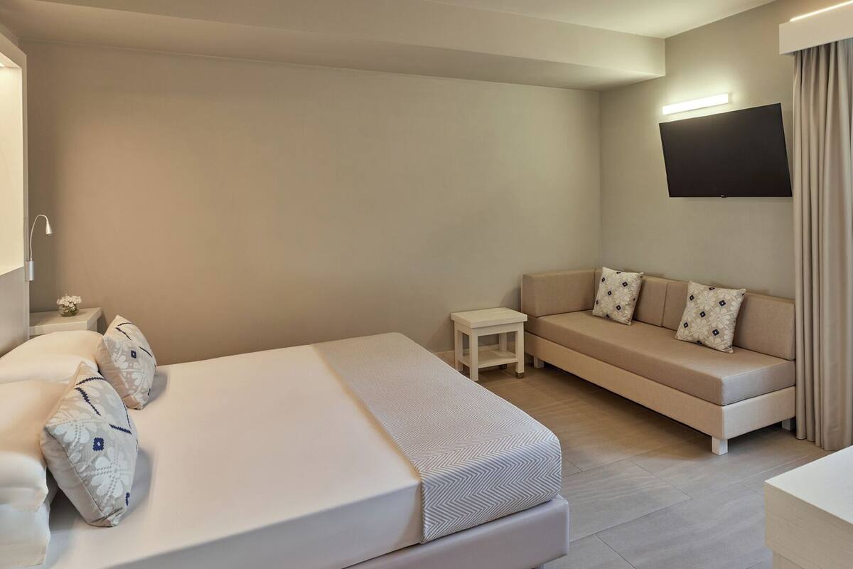 Een moderne hotelkamer met een bed, een bank, een klein tafeltje en een aan de muur bevestigde televisie.