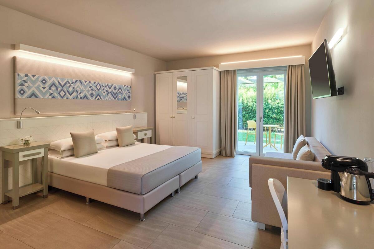 Een moderne hotelkamer met een groot bed, een sofa, een bureau met een waterkoker en een televisie.