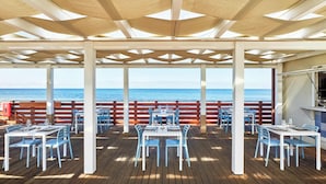 Un espace extérieur aménagé pour les repas, avec des tables et des chaises, une terrasse en bois et une vue sur l’océan.