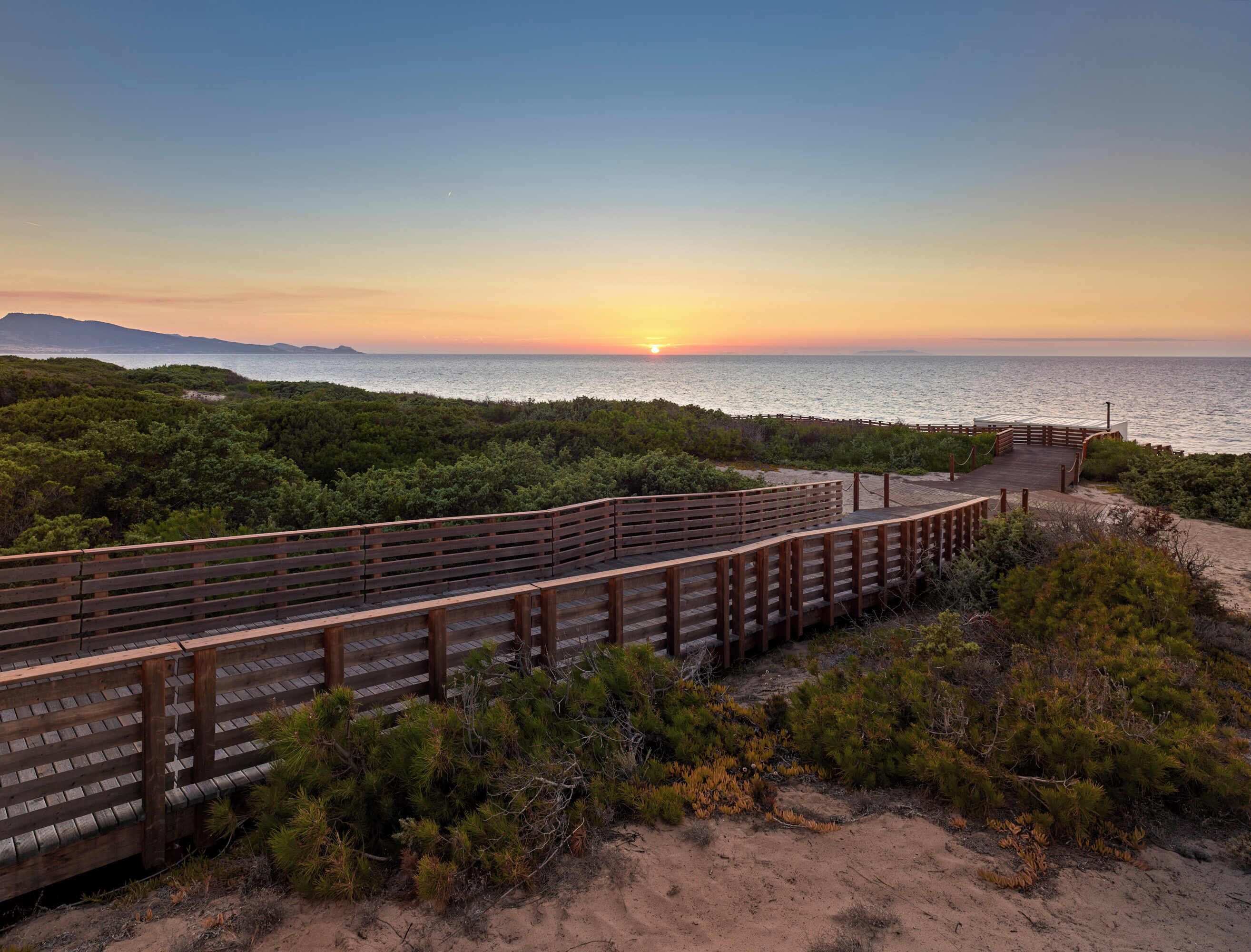 A wooden boardwalk leading to a beach with a sunset in the background.