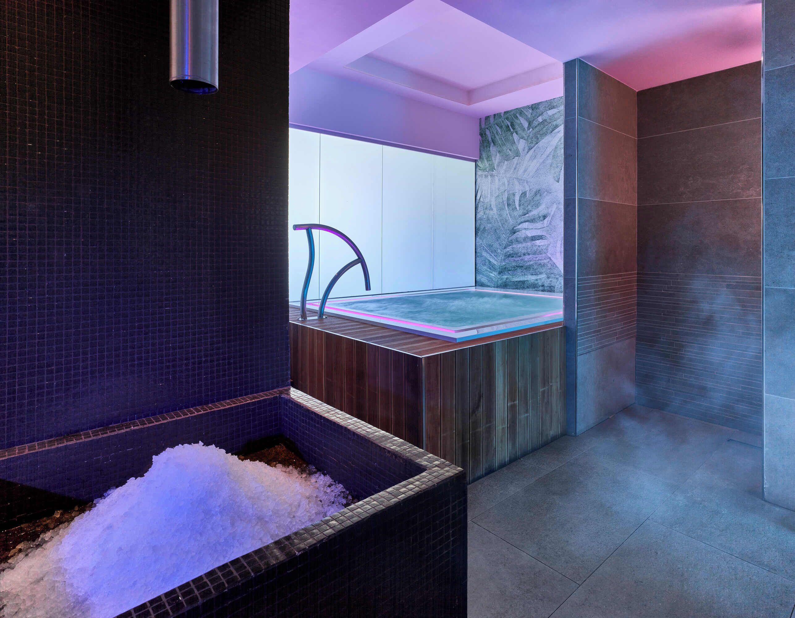 Un espace spa moderne doté d’un plancher chauffant, d’un grand bain d’eau glacée et offrant une vue sur la ville.