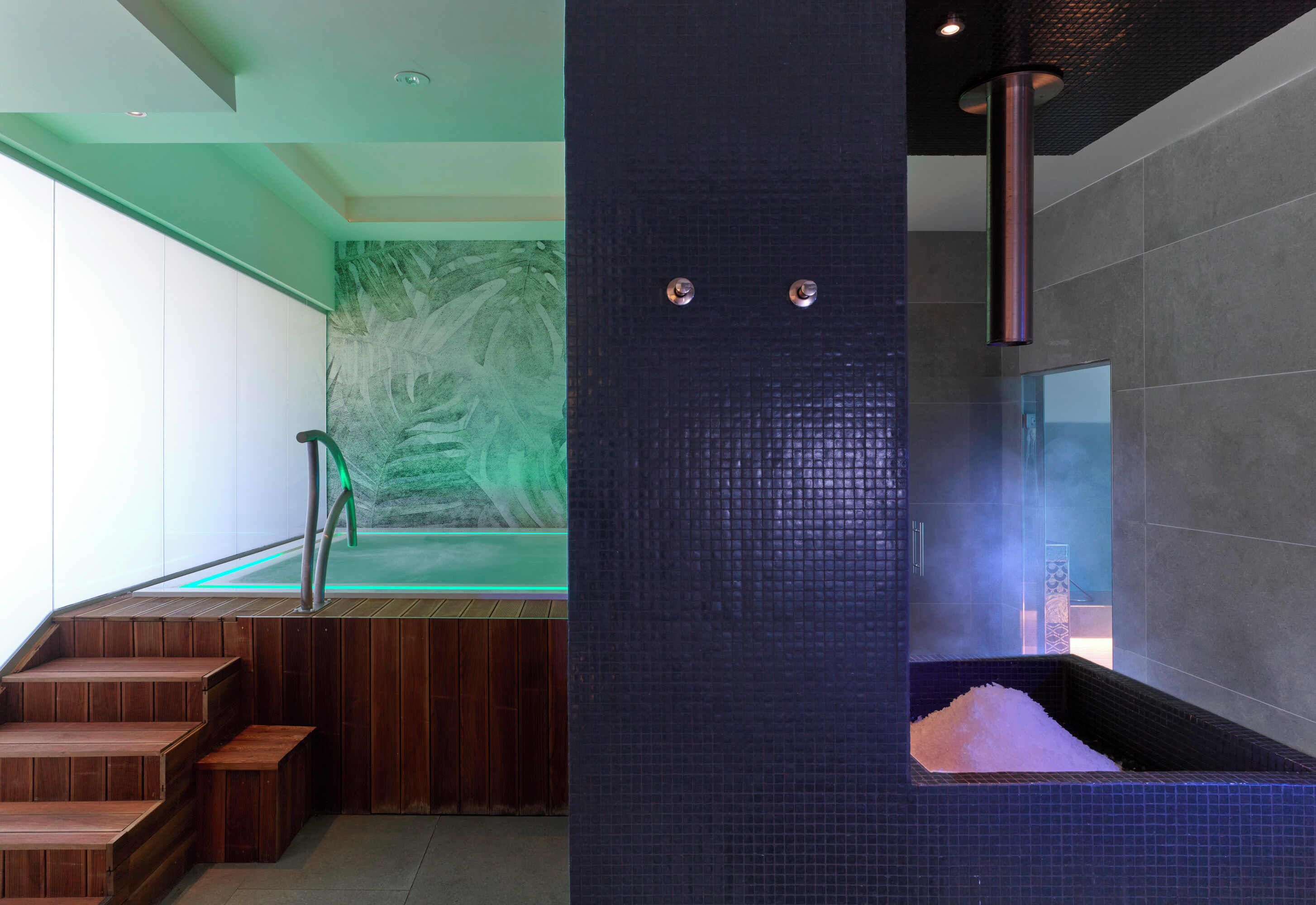 Et moderne spa-område med en trappe i træ, et stort, opvarmet kar og en grøn væg med abstrakt kunst.