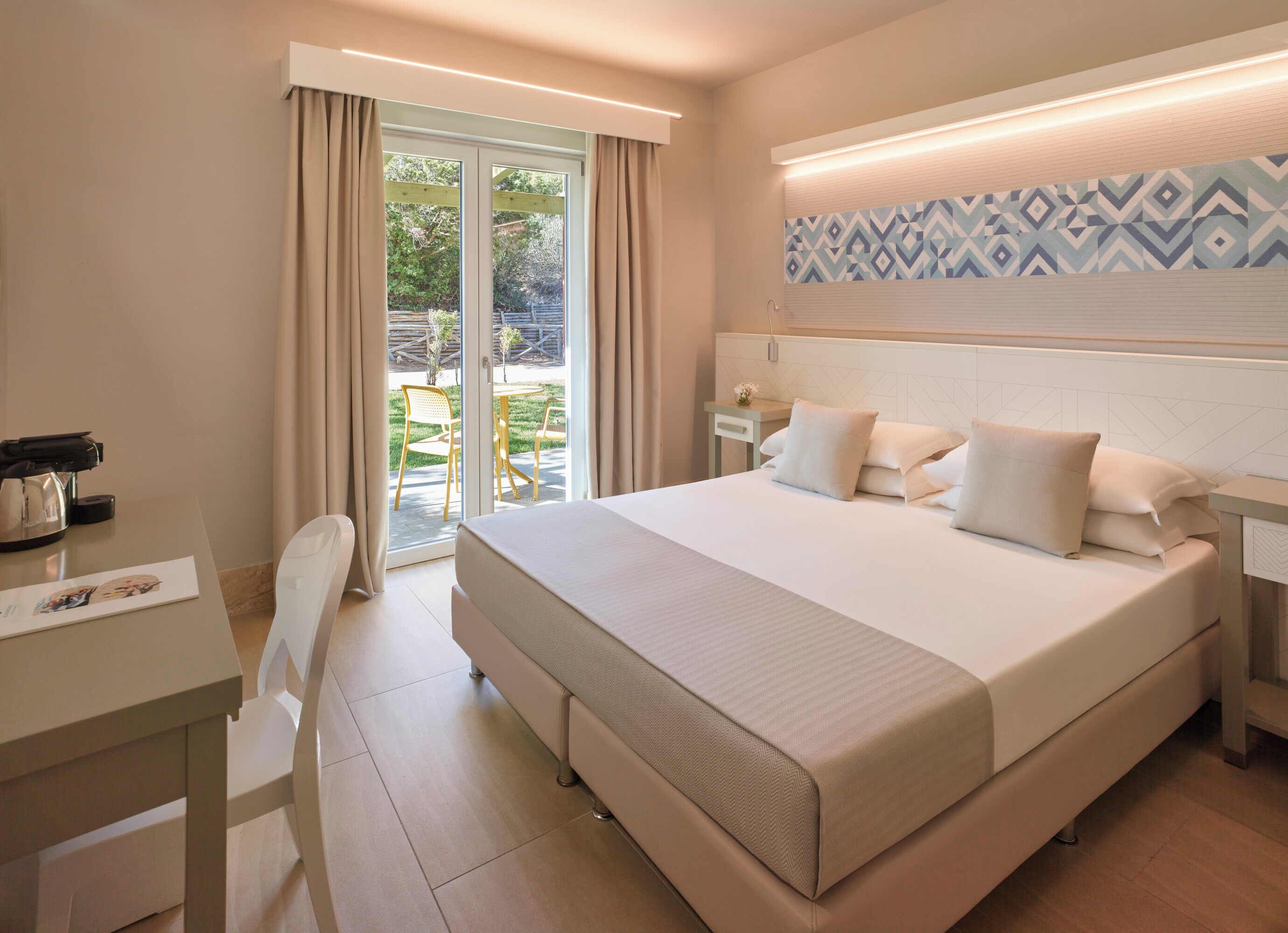 A hotel room with a large bed, a desk with a coffee maker, and a view of the outdoor patio.