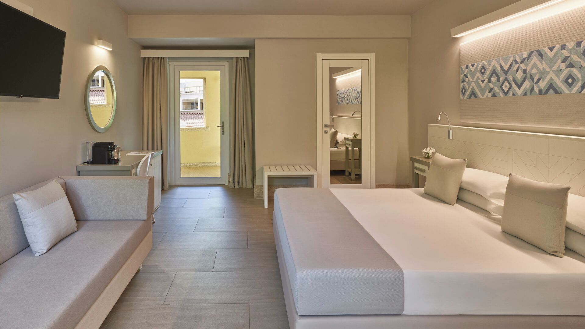Ein Hotelzimmer mit einem großen Bett, einer Couch, einem kleinen Tisch, einem Fernseher und einem durch eine offene Tür einsehbaren Badezimmer.