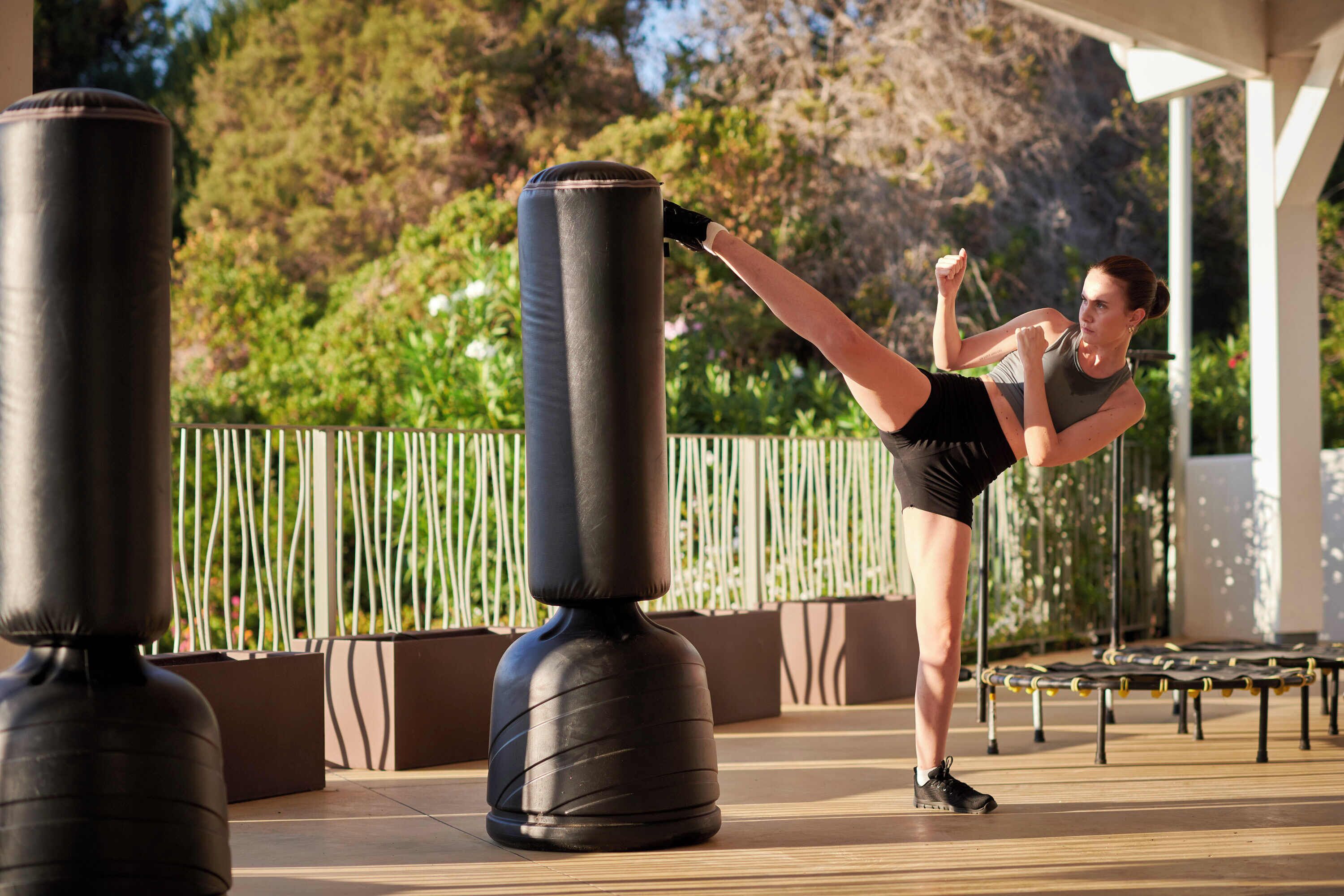 Una persona golpeando un saco de boxeo negro grande al aire libre.