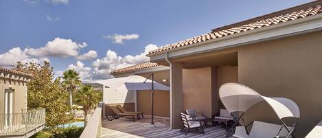A covered outdoor seating area with chairs and a table, a pool in the background, and a clear sky.