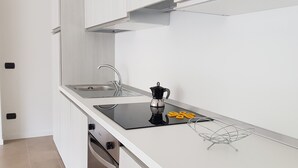A modern kitchen with a stainless steel sink, a black induction cooktop, and a coffee maker. - Vista Lago Spettacolare (Abbadia Lariana)