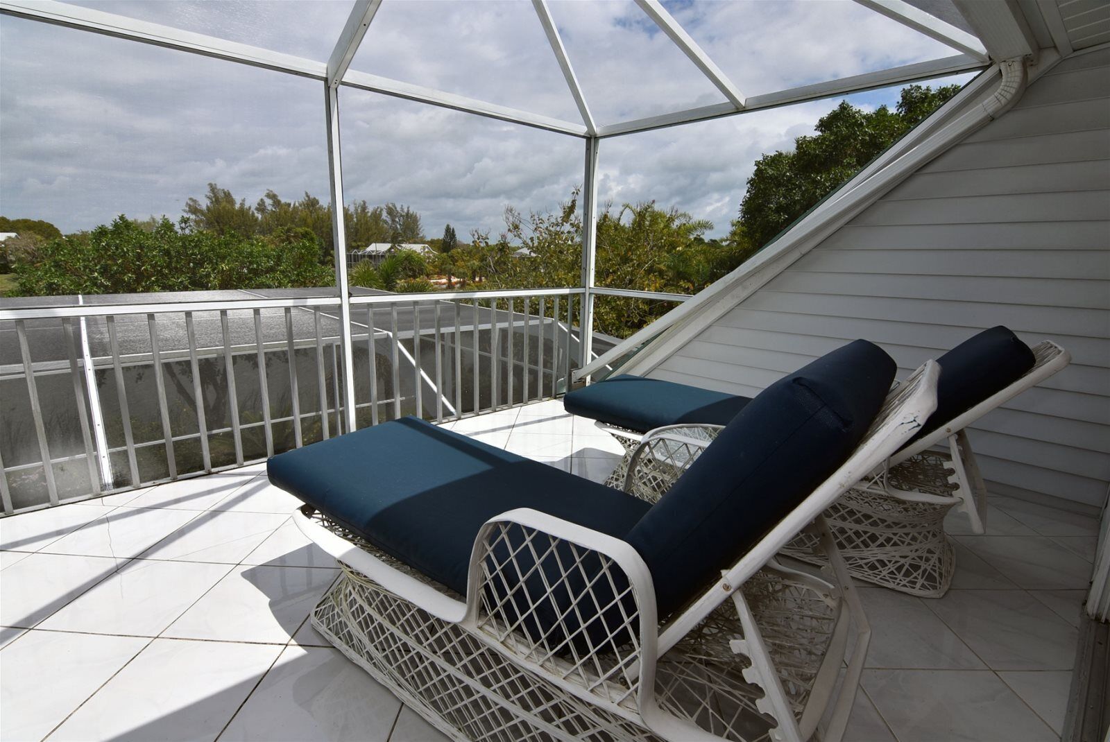 A covered outdoor area with two lounge chairs and a white railing.