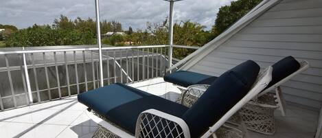A covered outdoor area with two lounge chairs and a white railing.