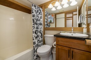 A bathroom with a white toilet, a shower curtain with animal prints, a wooden vanity with a sink, and a mirror above the vanity. - Gold Bend 5111 - Stylish Dog Friendly Condo on Shuttle Route with HOA Gym and Hot Tub Access (Truckee)
