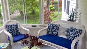 Una veranda con mobili in vimini, un tavolo verde e vista su un giardino.