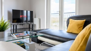 Una sala de estar moderna con un televisor de pantalla plana, un sofá, una mesa de centro de vidrio y una planta en maceta.