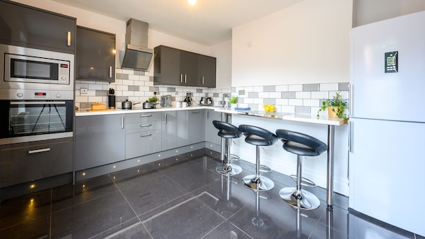 Una cocina moderna con electrodomésticos de acero inoxidable, salpicadero de azulejos y una barra con taburetes.