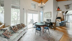 A spacious living room with a wooden ceiling, a round dining table, and a sofa with patterned cushions.