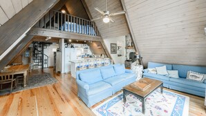 A spacious loft with a high ceiling, wooden beams, a blue sofa, a wooden coffee table, and a kitchen area.