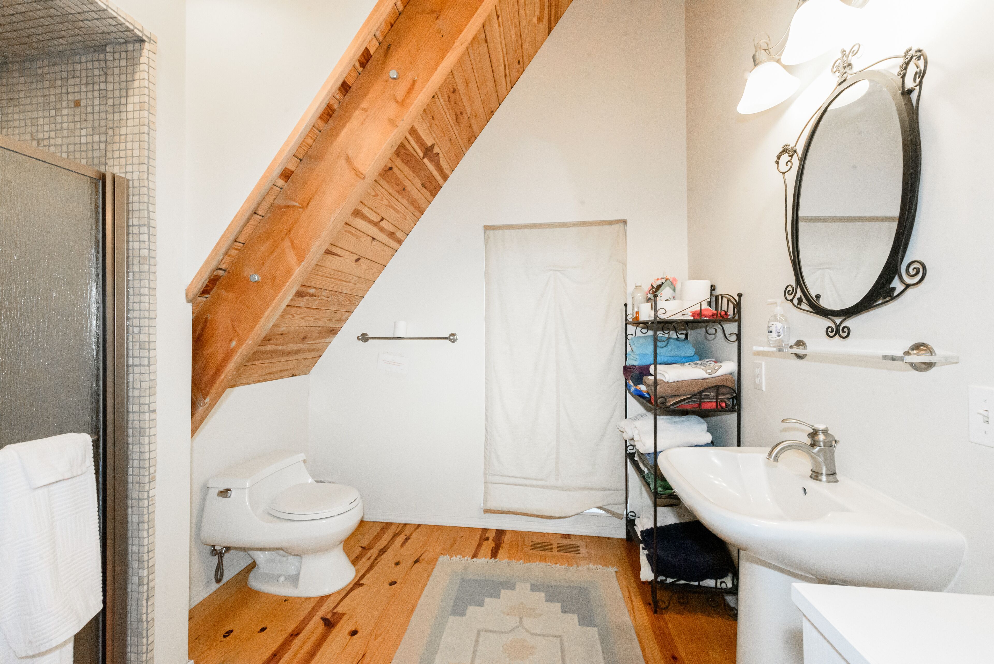 Bagno con soffitto in legno, un water bianco, un lavandino, uno specchio e un porta asciugamani.