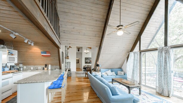 A spacious kitchen with a central island, a dining area with a sofa and table, and large windows offering a view of the outdoors.