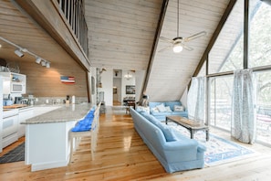 Una cocina amplia con una isla central, un comedor con sofá y mesa, y ventanas grandes que ofrecen vistas al exterior.
