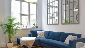 A room with a blue sofa, a large window, a radiator, and a potted plant. - 3 bedroom accommodation in Ramsgate (Ramsgate)
