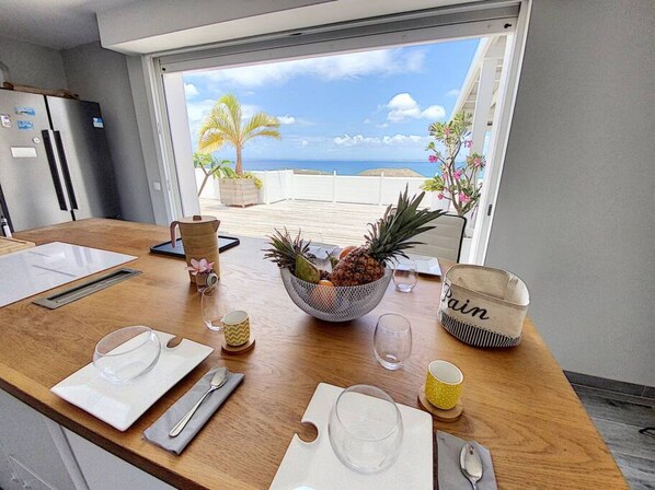 A dining table set with plates, cutlery, and a bowl of fruit. - Villa La Guapa sea view private pool 5 min from the beach (La Savane)