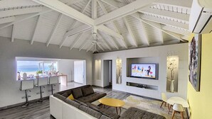 A spacious living area with a large sectional sofa, a television mounted on the wall, and a dining area with bar stools. - Villa La Guapa sea view private pool 5 min from the beach (La Savane)