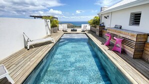 A pool area with a wooden deck, lounge chairs, and a view of the ocean. - Villa La Guapa sea view private pool 5 min from the beach (La Savane)