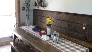 Une table à manger en bois, recouverte d’une nappe à carreaux, avec des bancs, un lustre et un panneau mural sur lequel on peut lire : « RASSEMBLEZ VOS AMIS ET VOTRE FAMILLE ».