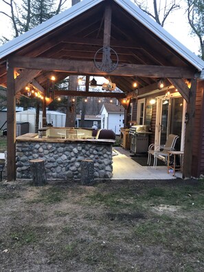 A covered outdoor kitchen area with a stone countertop, wooden stools, and string lights.