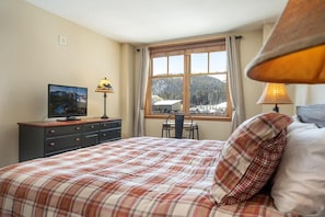 Une chambre à coucher comprenant un lit, une télévision, un bureau et une fenêtre donnant sur un paysage enneigé.