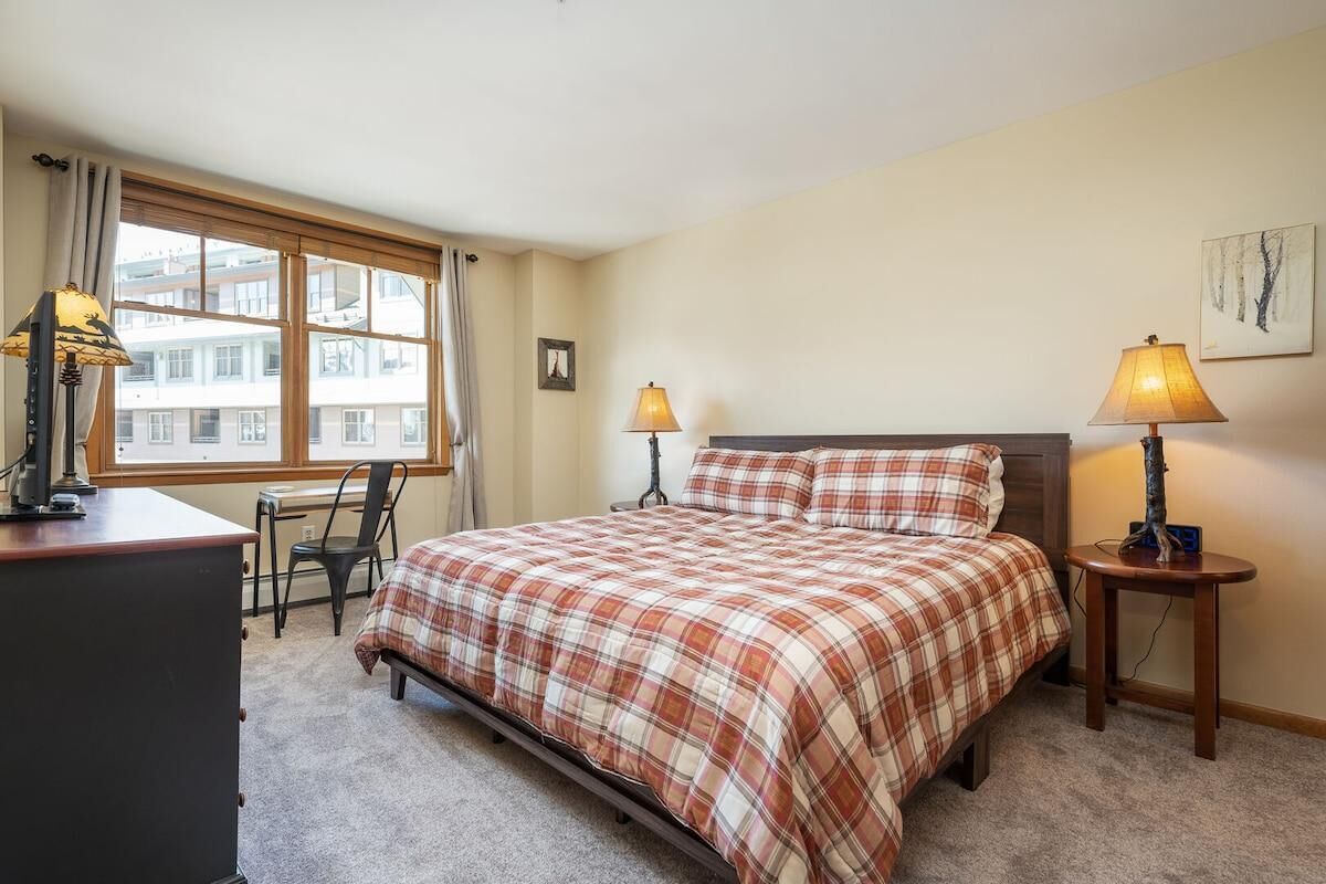 A bedroom with a bed, two bedside lamps, a desk, and a chair.