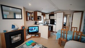 A compact living space with a television, kitchenette, dining area, and a fireplace. - Top-of-the-range mobile home (Dinard)