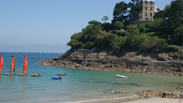 A coastal scene with a historic building on a cliff, clear blue water, and several boats. - Top-of-the-range mobile home (Dinard)