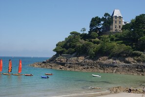 A coastal scene with a historic building on a cliff, clear blue water, and several boats.