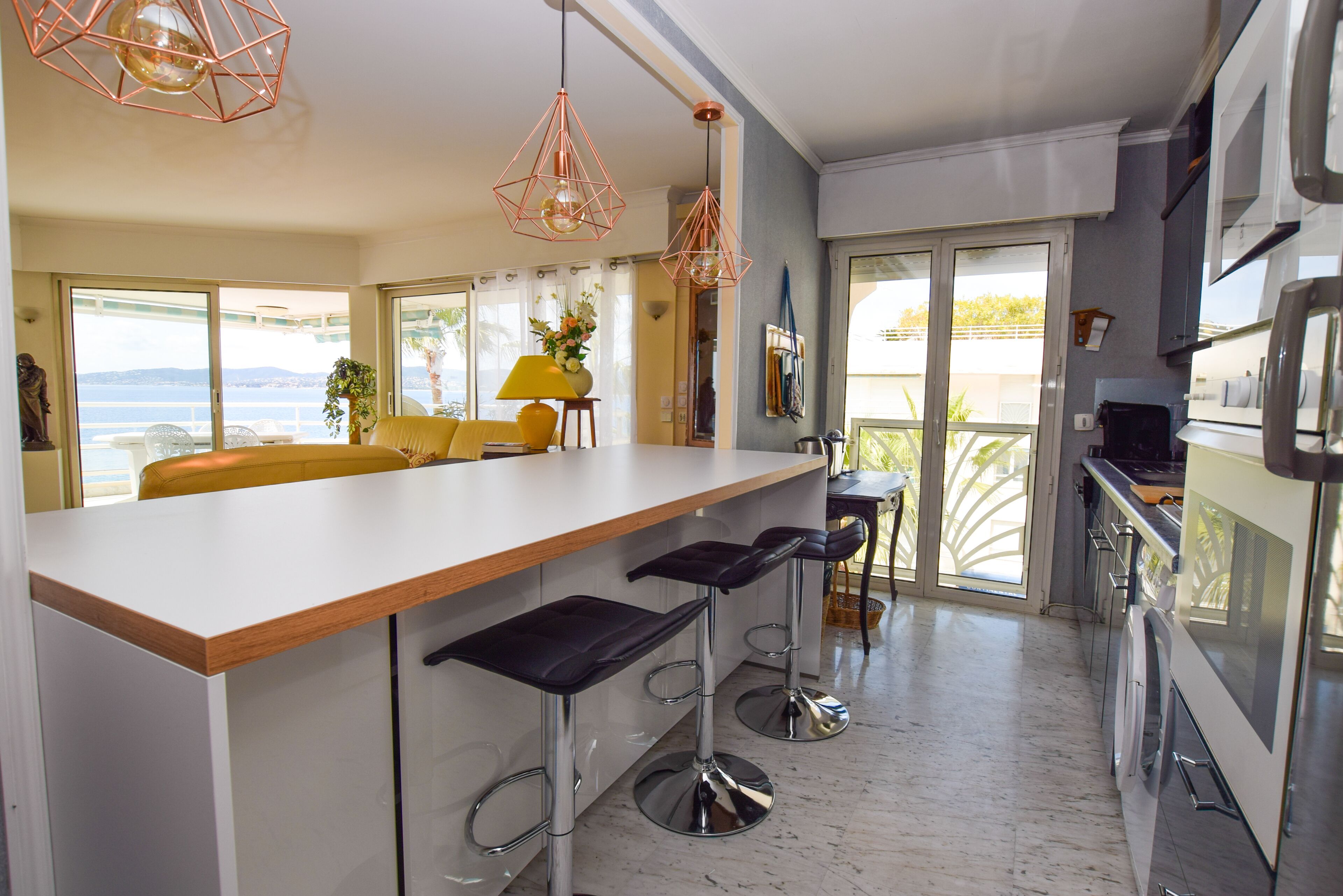 Een moderne keuken met een centraal eiland, een paar barstoelen en uitzicht op zee.
