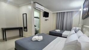 Habitación de hotel con dos camas, un escritorio, un espejo, un televisor y un equipo de aire acondicionado.