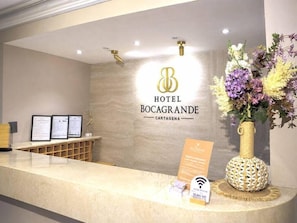 A hotel reception desk with a logo, framed documents, a vase of flowers, and a Wi-Fi sign.