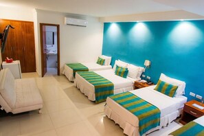 Camera d'albergo con tre letti, un divano, un bagno e una parete di colore blu.