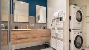 Uma casa de banho moderna com uma pia dupla, toucador de madeira, um espelho, um porta-toalhas e uma máquina de lavar roupa com abertura frontal.
