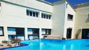 A swimming pool with a blue interior, surrounded by a building with a reception and bar area. - Duplex en Bord de mer Dans Residence Avec Piscine (CALCATOGGIO)