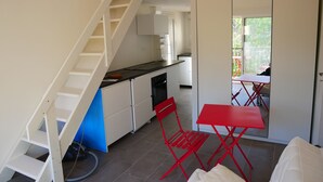 A compact kitchen with white cabinets, a red folding table, and a red chair. A staircase leads to a balcony with a red table and chairs. - Duplex en Bord de mer Dans Residence Avec Piscine (CALCATOGGIO)