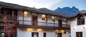 A traditional building with a balcony, multiple windows, and a mountainous backdrop. - Hotel Private Collection R House Cusco (Calca)