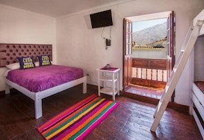 A bedroom with a bed, a colorful striped rug, a television on the wall, and a balcony with a view. - Hotel Private Collection R House Cusco (Calca)