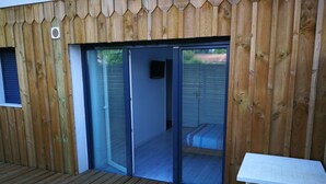 A wooden deck with a sliding glass door leading to a room with a bed and a small table. - Self-contained apartment, patio with terrace and bicycle paths (La Teste-de-Buch)