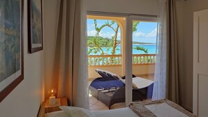 Una camera d'albergo con un letto, un tavolino con una lampada e vista sulla spiaggia e sull'oceano attraverso una porta scorrevole.