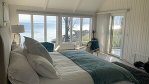 Une chambre à coucher avec un grand lit, une vue sur la mer et un violon appuyé contre le mur.