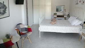 A bedroom with a bed, bedside table, chair, and a TV mounted on the wall. - George place two-storey holiday home offers panoramic sea and mountain views. (Λυγαριά)
