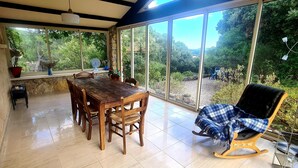 Un comedor con una mesa y sillas de madera, una mecedora y vistas a un jardín a través de amplios ventanales.